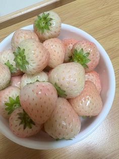 a white bowl filled with strawberries on top of a wooden table