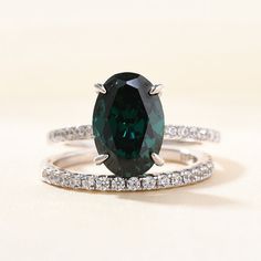 an oval cut green diamond ring with white diamonds on the sides and two bands around it