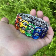 a hand holding several different colored bracelets in it's palm, with grass in the background