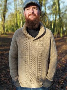 a man with a beard wearing a sweater and hat standing in the woods looking up