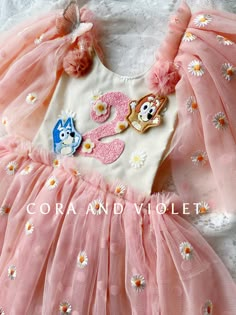 a pink and white dress with two cartoon characters on the front, sitting on a lace doily