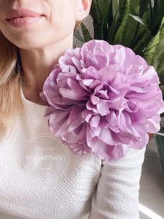 a close up of a person holding a large flower in front of her face and smiling at the camera