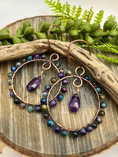 a pair of hoop earrings with purple and green beads on top of a piece of wood