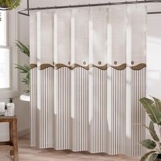 a white shower curtain with brown trim in a bathroom next to a potted plant