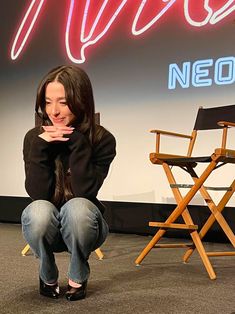 a woman sitting on the ground in front of a chair with her hand over her mouth