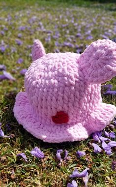 a crocheted pink teddy bear laying in the grass with purple flowers around it