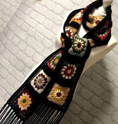 a black scarf with multicolored crocheted flowers on it sitting on top of a white mannequin