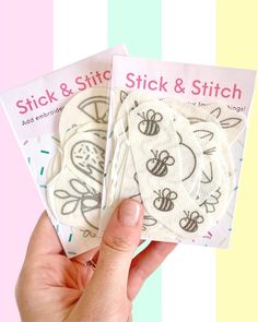 two stick and stitch patches in the palm of a person's hand, on a multi - colored striped background