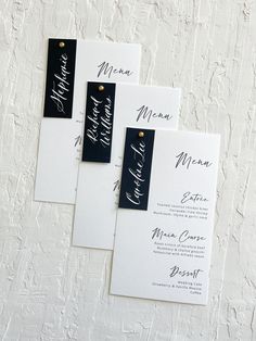 three black and white wedding stationery cards with calligraphy on them, sitting on a table