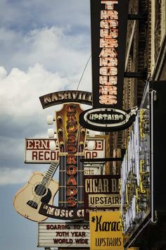 many signs are hanging on the side of a building in front of a guitar shop