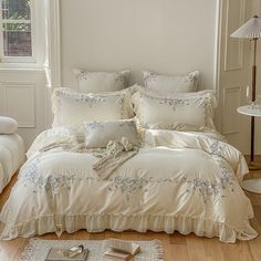 a white bed sitting in a bedroom next to a lamp and pillows on top of a wooden floor