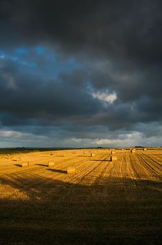 an open field with bales of hay under a cloudy sky and dark clouds above