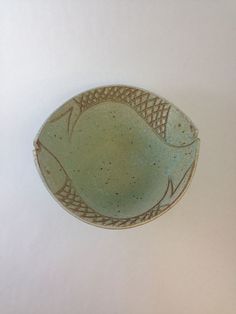 a green bowl with fish on it sitting on a white counter top next to a knife and fork