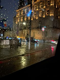 rain is falling on the window and cars are driving down the street in the city at night