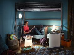 a young man sitting on top of a bunk bed next to a table and lamp