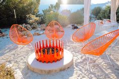 four orange chairs sitting on top of a sandy beach next to an umbrella covered gazebo