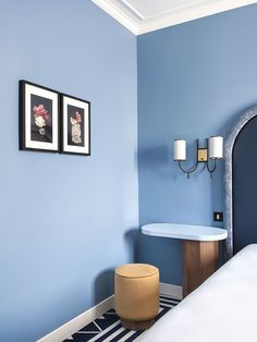 a bedroom with blue walls and two pictures on the wall next to a white bed