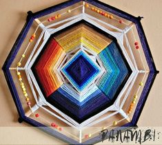 a multicolored paper art work on the wall with string and beads hanging from it's sides