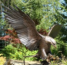 a statue of an eagle with its wings spread out in front of trees and bushes