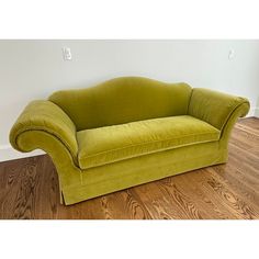 a green couch sitting on top of a hard wood floor next to a white wall