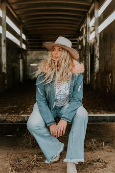 a woman sitting on the ground wearing jeans and a hat with her hair blowing in the wind