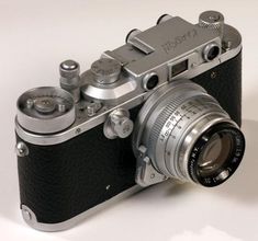 an old fashioned camera sitting on top of a white table next to a black and silver lens