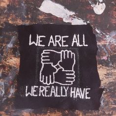 An unevenly cut, square, black fabric patch is on a paint-stained background. On the patch, there is an image of four hands in an interlocked square. Above the hands, there are the words, in all caps, "We Are All", beneath the hands in all caps are the words "We Really Have". Patch Design Ideas Punk, Punk Pins And Patches, Folk Punk Patches, Punk Patch Stencil, Punk Patches Diy Ideas, Punk Diy Ideas, Punk Patch Ideas, Punk Embroidery Ideas