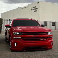 a red chevrolet truck parked in front of a white building with black lettering on it