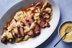 a white plate topped with meat covered in gravy next to a bowl of sauce