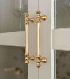 two golden handles on a white door with wine glasses in the glass case behind them