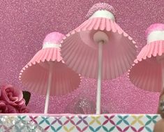 two pink paper umbrellas sitting on top of a table next to a vase with flowers