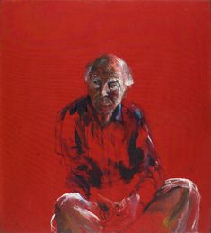 an older man sitting on the ground in front of a red wall