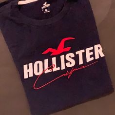 Embroidered Lettering On The Front With The Traditional Logo From Hollister. Soft Feel, Never Worn. Navy Blue With White And Red Accents. Back Is Solid Blue - No Graphic. Hollister Shirts Men, Holster Shirt, Traditional Logo, Embroidered Lettering, Hollister Shirts, Embroidered Tshirt, Red Accents, Blue T, T Shirt And Shorts