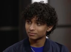 a close up of a person wearing a blue shirt and black jacket with curly hair