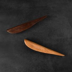 two wooden spoons sitting next to each other on a black surface with dark background