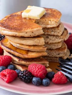 stack of pancakes with butter and berries on pink plate