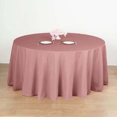 a round table with two white plates on it and pink flowers in vases at the top