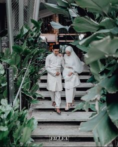 two people are walking down some steps in front of green plants and greenery on either side of them