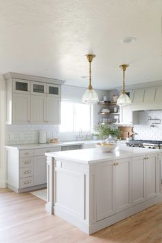 a large kitchen with white cabinets and wooden floors is pictured in this image, there are two pendant lights hanging over the island