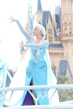 a woman dressed as disney princess in front of a castle with snow falling on her