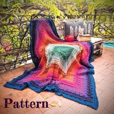 a colorful crocheted blanket sitting on top of a bench next to a tree