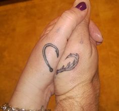 two people holding hands with tattoos on their fingers and one has a heart shaped arrow