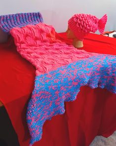 a pink and blue knitted blanket sitting on top of a bed