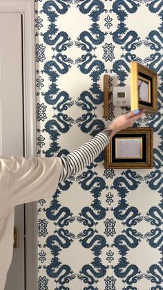 a person is holding something in front of a wall with blue and white designs on it