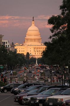 cars parked in front of the capitol building at sunset, with people walking on the sidewalk