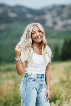 a woman standing in a field with her hands on her hips and smiling at the camera