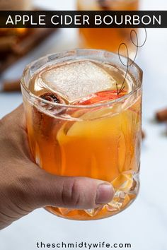 a hand holding a glass with an apple cider bourbon