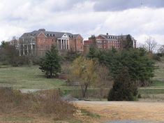 a large brick building sitting on top of a lush green field next to a forest