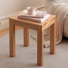 a small wooden table with a book and cup on it in front of a couch