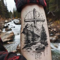 a man with a cross tattoo on his arm next to a river and mountain range